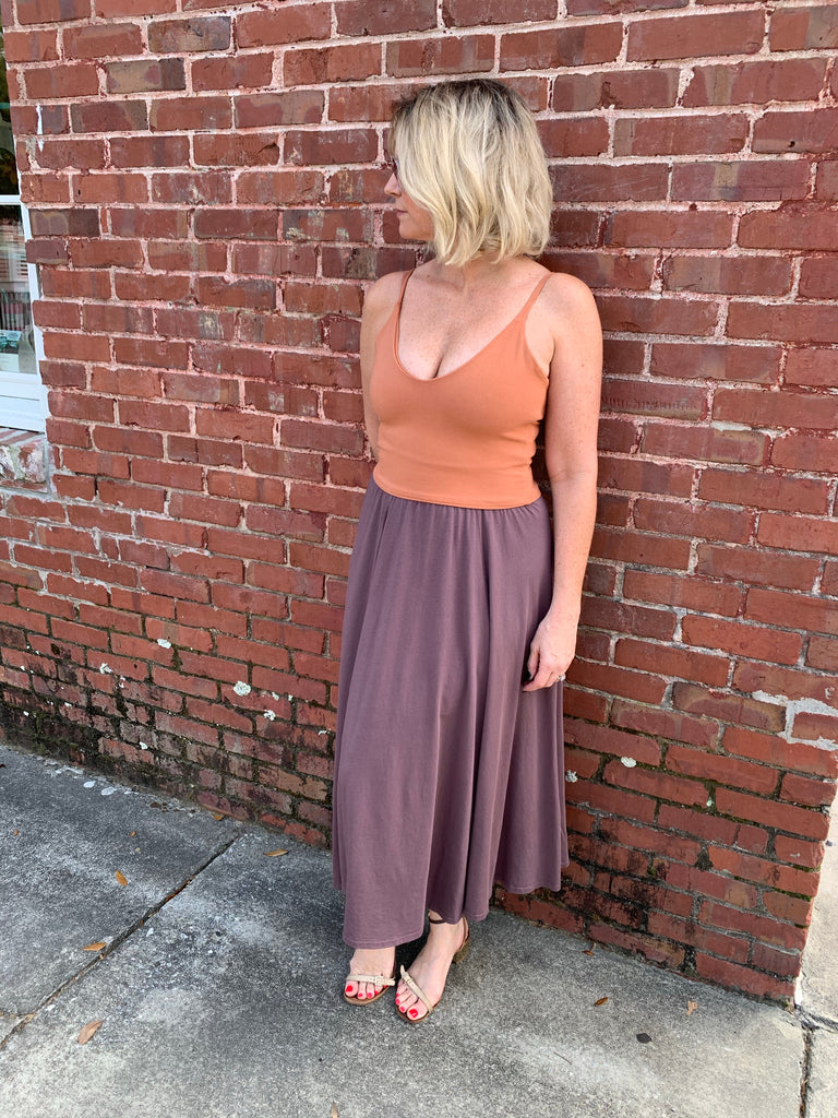 woman leaning on red brick wall wearing orange crop top and purple skirt